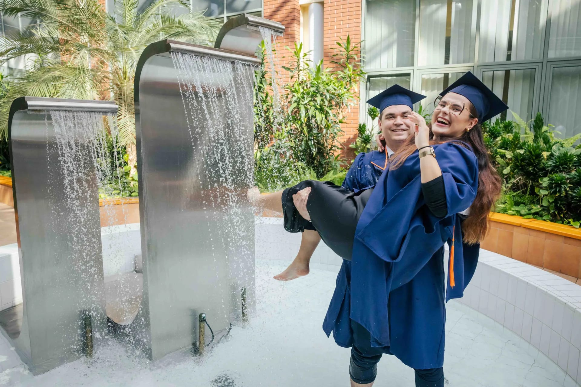 Student trzyma na rękach studentkę w fontannie na dziedzińcu uczelni