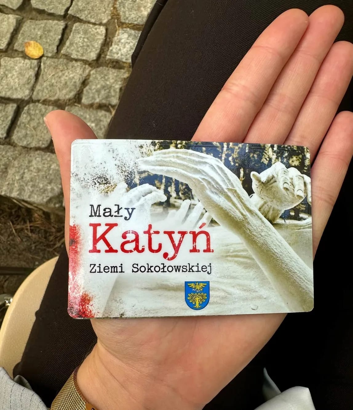 Na dłoni leży ulotka z napisem Mały Katyń